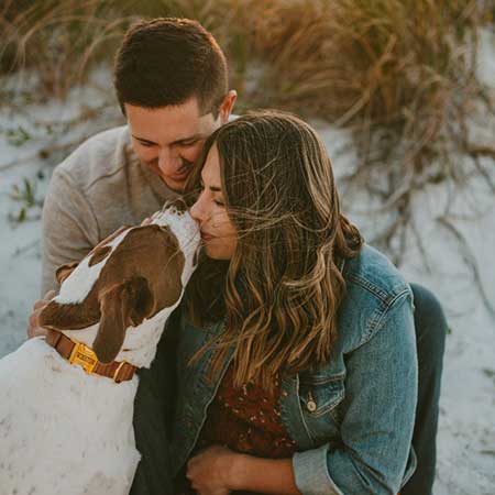 man en vrouw knuffelen met een hond op de duinen